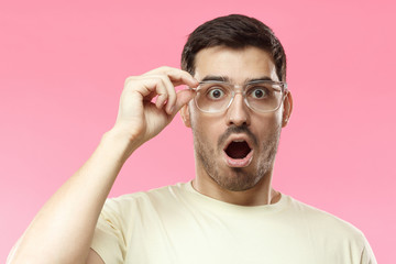 Casual dressed young man in beige t-shirt shouting oh my god with open mouth, surprised by low...