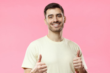 Young optimistic man isolated on pink background showing thumbs up with positive emotions of content and happiness. Concept of satisfaction with quality and recommendation