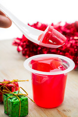 Delicious strawberry jelly and xmas gift box on wooden table. Sweet fruity pudding in transparent cup.