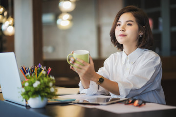 Businesswoman working on laptop while drinking coffee in the office