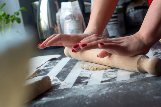 Woman rolling dough for pasta at the kitchen wooden table, she have nice red nails. 