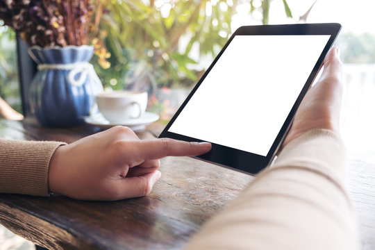 Mockup image of a woman holding black tablet pc with blank white desktop screen in cafe