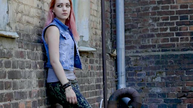 Teenage girl with nose piercing and pink hair standing on brick wall background. Slow motion. HD