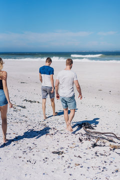Group of young friends walking barefoot on a beach