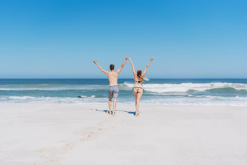 Joyful young couple running towards the ocean