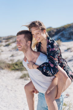 Happy loving couple piggy back riding at a beach