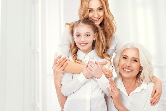 A happy family is a home. Family portrait of a mature woman standing embracing her adorable daughter and charming mother while all wearing matching attires and posing for the camera.