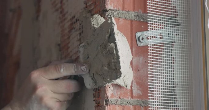 Slow motion handheld shot of worker applying plaster on the wall near window