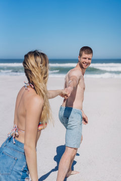 Young man pulling his girlfriend across a beach