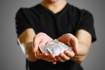 Man's hand holding three condoms. Close up. Isolated on grey background
