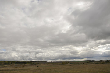 Heavy grey clouds in the cold autumn sky over fields, forests and mountains