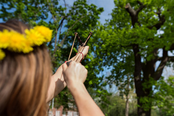 Girl shooting from the professional wooden slingshot in the park during a sunny day