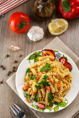 Vegetarian vegetable pasta Fusilli with tomato, parsley and olive oil in white plate on wooden table.