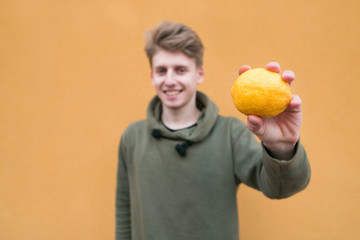 Happy man standing on an orange background with lemon in his hands. Focus on lemon.