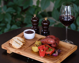 Grilled sausages with vegetables, tomatoes, onion, potatoes and mushrooms on the wooden board served with a glass of  red wine.