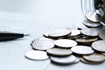 Business, finance, saving money or investment concept : Coins scattered from glass jar, pen and savings account passbook or financial statement on office desk table