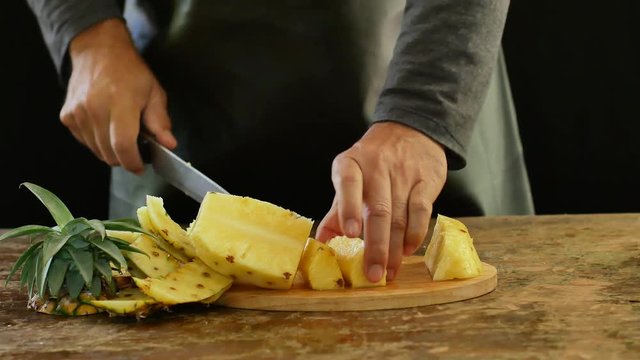 hands cutting pineapple on a cutting board on a wooden table. 