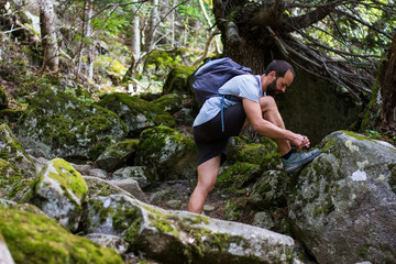 Naklejka na ściany i meble man tying his shoes during a walk in the woods