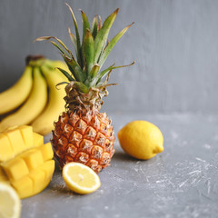Yellow fruits. Ripe juicy pineapple with mango, banana and lemons on gray wooden table