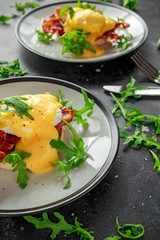 Eggs Benedict on english muffin with crispy bacon, wild rocket salad and hollandaise sauce.