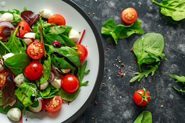 Fresh Cherry Tomato, Mozzarella salad with green lettuce mix and red onion. served on plate. healthy food.