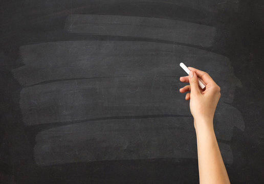 Female hand holding white chalk in front of a blank blackboard