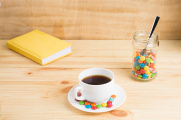 Coffee mug, colored candy in a jar and a yellow diary on a wooden background. breakfast or lunch