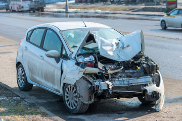 a white car with a broken front on the road in the city