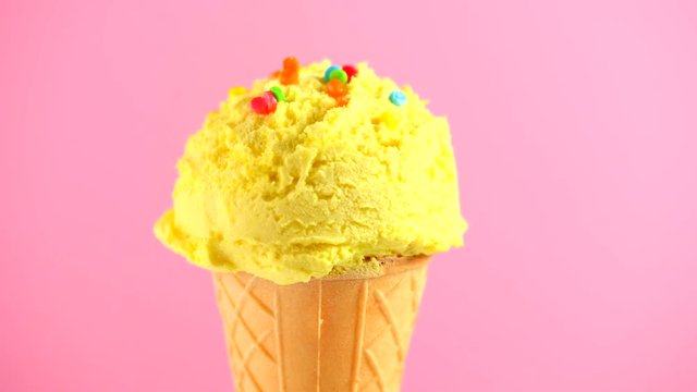 Ice cream. Vanilla, banana or lemon flavor icecream in waffle cone rotated over pink background. Sweet dessert decorated with colorful sprinkles closeup. 4K UHD video footage. 3840X2160