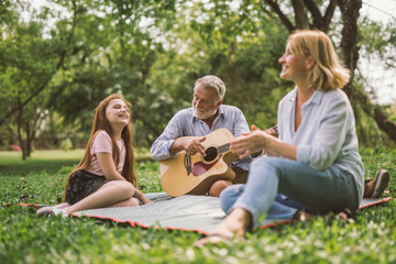 family enjoying quality time, playing guitar in their green park garden.