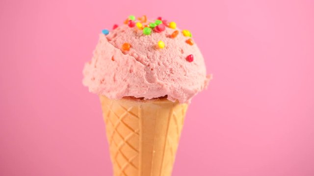 Ice cream. Strawberry or raspberry flavor icecream in waffle cone rotated over pink background. Sweet dessert decorated with colorful sprinkles closeup. 4K UHD video footage. 3840X2160