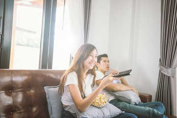 Couple on sofa with TV remote watching television in living room