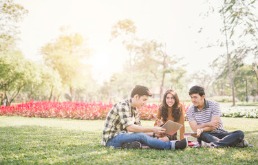 happy students sitting and tutoring with tablet screen each other in a campus at park with a warm...