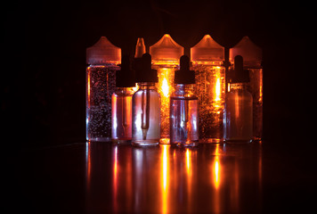Vape concept. Smoke clouds and vape liquid bottles on dark background. Light effects