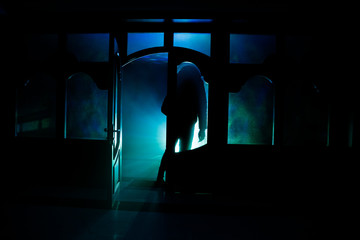Silhouette of an unknown shadow figure on a door through a closed glass door. The silhouette of a human in front of a window at night. Scary scene halloween concept of blurred silhouette
