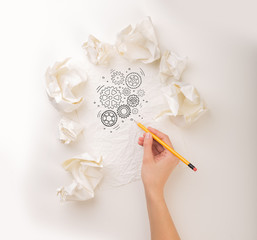 Female hand next to a few crumpled paper balls drawing rotating gears