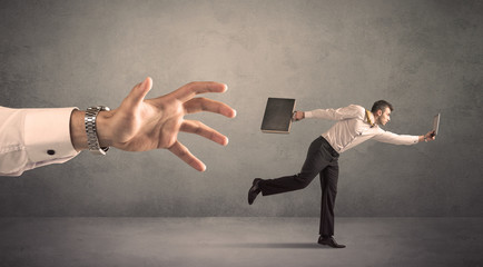 Young miniature businessman running from a big hand with grey background