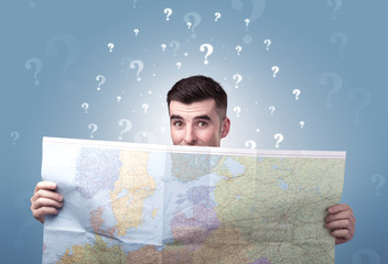 Handsome young man holding a map with white question marks above his head