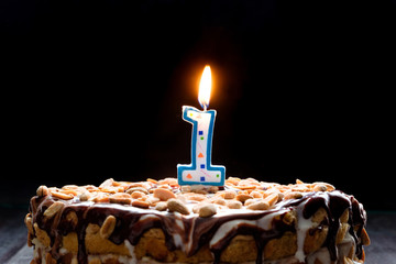 One flaming candle on birthday cake on black background