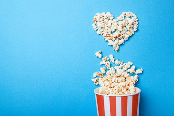 I like watching films. Spilled popcorn in the shape of heart and paper bucket in a red strip on...