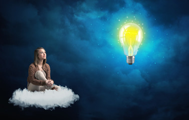 Caucasian woman sitting on a white fluffy cloud looking and wondering at a big, bright, shiny, glowing yellow lightbulb