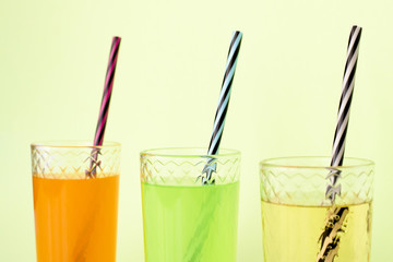 Transparent glass glasses with straws and orange, lime and pear lemonade on green background. The...