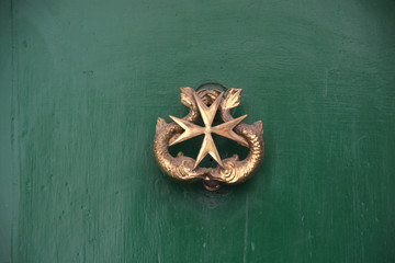 złota kołatka do drzwi w kształcie krzyża maltańskiego na zielonych drzwiach - obrazy, fototapety, plakaty