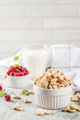 Healthy breakfast ingredients. Breakfast cereal corn rings, milk or yogurt glass, raspberries and mint on grey stone background, copy space