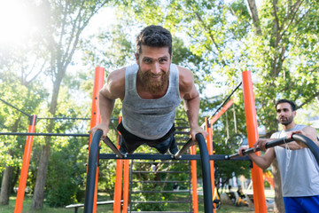 Low-angle view of an athletic bearded young man doing push-ups on parallel horizontal bars during...
