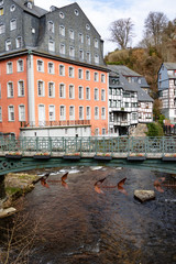 Rathaus mit roter Fassade und davor liegender Brücke über einen Fluss in der Innenstadt von Monschau in der Eifel