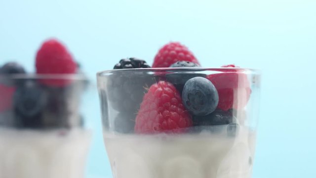closeup of turning glasses with some white dessert mouse panna cotta yogurt decorated with berries on light blue background
