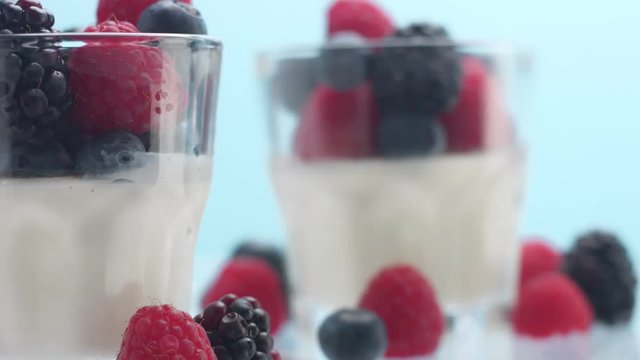 closeup of turning glasses with some white dessert mouse panna cotta yogurt decorated with berries on light blue background
