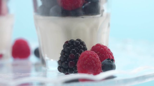 closeup of turning glasses with some white dessert mouse panna cotta yogurt decorated with berries on light blue background