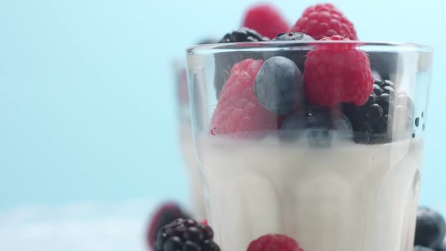 closeup of turning glasses with some white dessert mouse panna cotta yogurt decorated with berries on light blue background